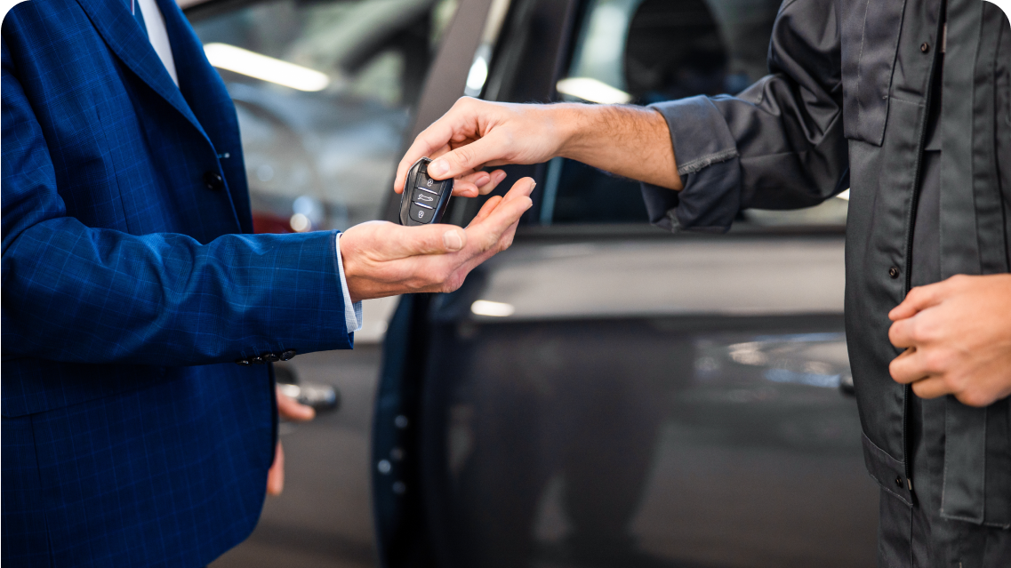 Person in suit receiving car key from worker near vehicle